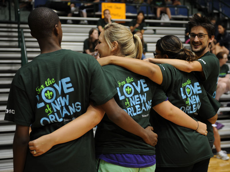 Four students show off the backs of their t-shirts and share a hug at Outreach event